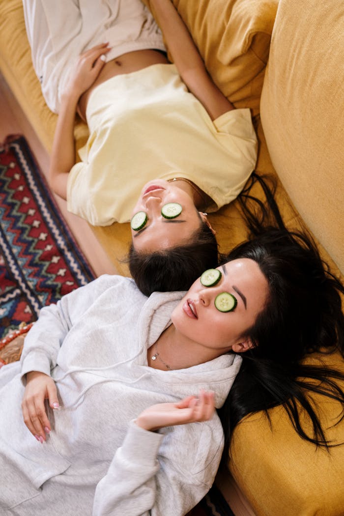 our-story-01 Two women enjoying a relaxing spa day with cucumber masks in a cozy home setting.